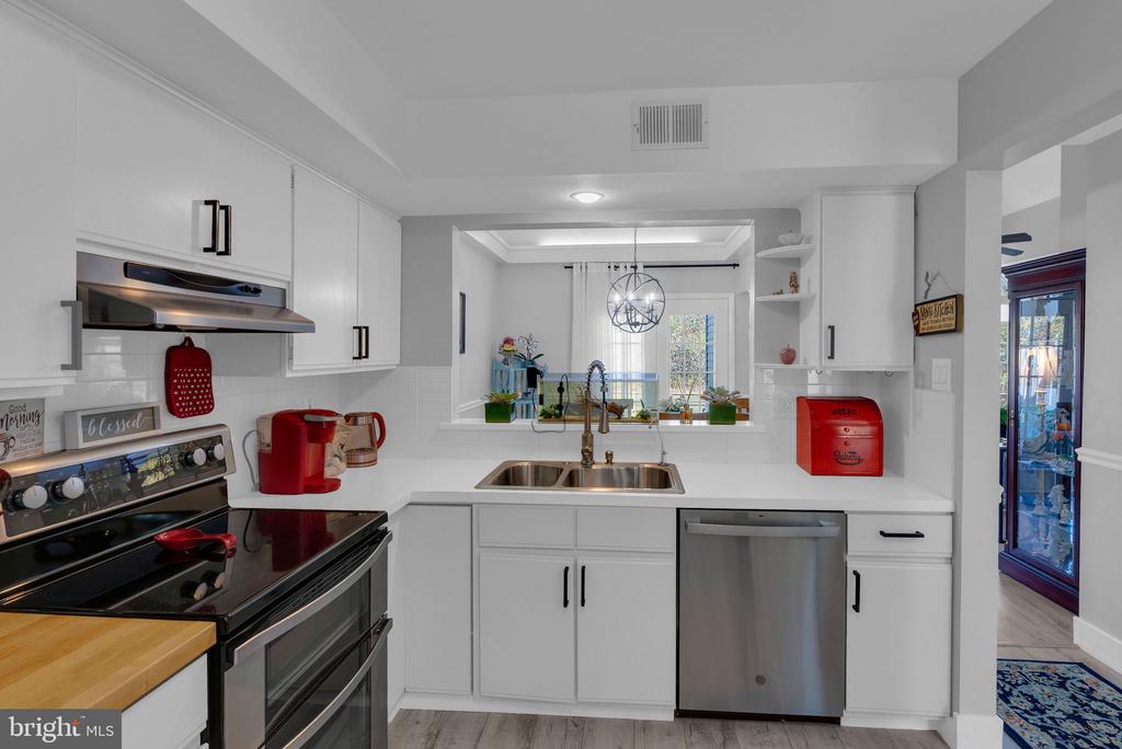 White kitchen with stainless steel appliances, a double-basin sink, and a pass-through to the dining area.