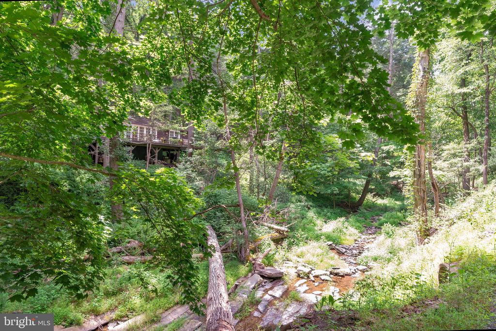 Wooded home beside a rocky creek, with a raised deck partly hidden among trees.