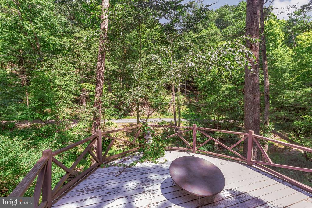 Wooden deck with a round metal table, surrounded by leafy trees.