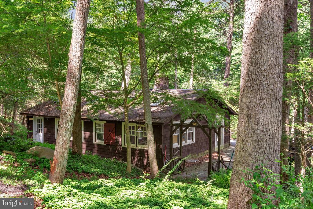 Wooded home with dark shingle siding and a covered porch among mature trees.