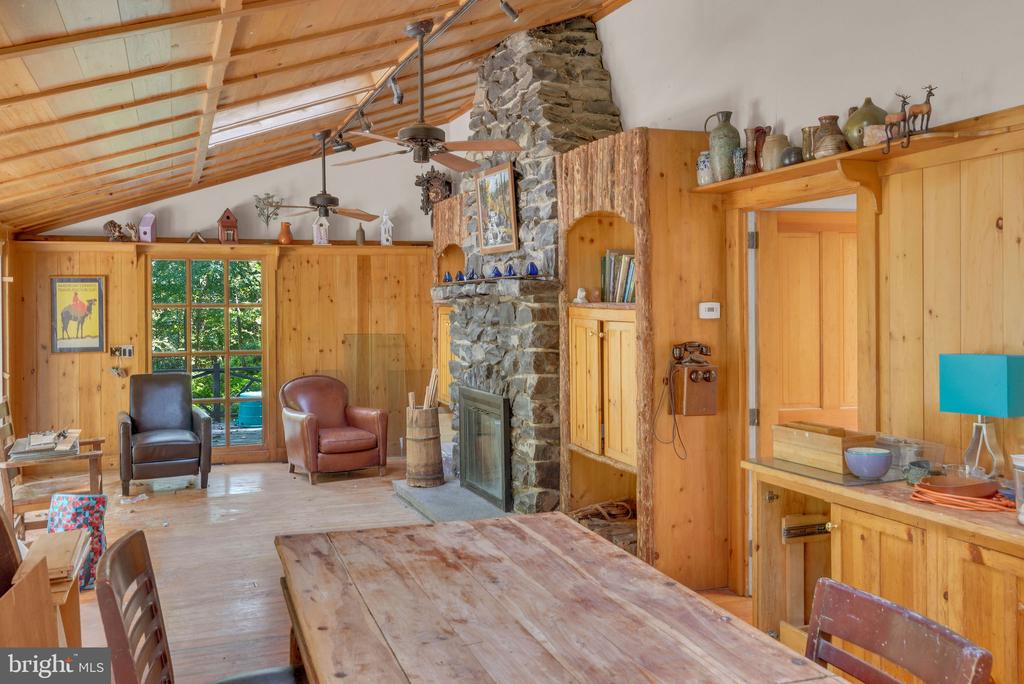 Rustic dining and living area with a long wooden table, timber ceiling, and stone fireplace.