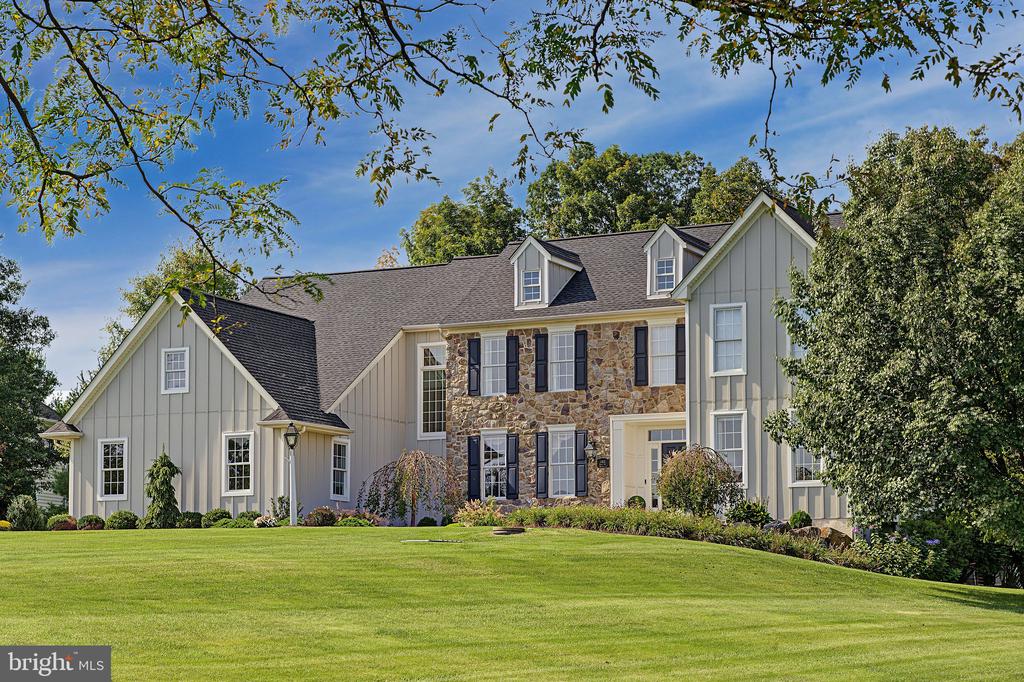 Large home with a stone facade, gray siding, and dormers behind a broad green lawn.