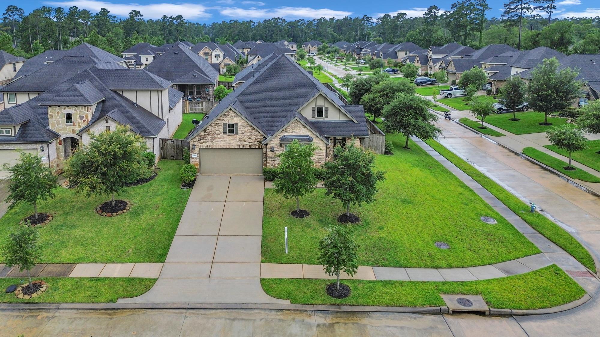 Aerial view of a brick-and-stone home with a wide driveway on a tree-lined residential street.