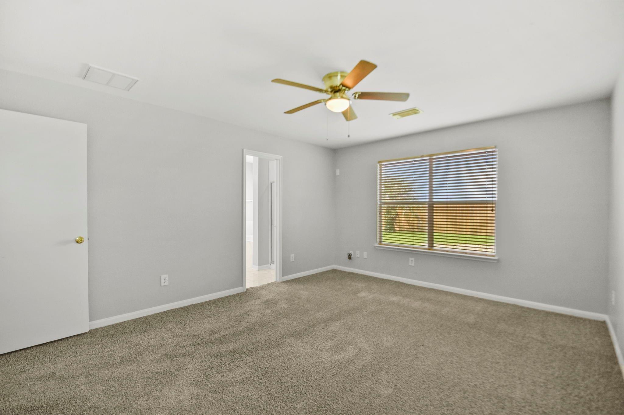 Empty bedroom with beige carpet, a ceiling fan, and a wide window with blinds.