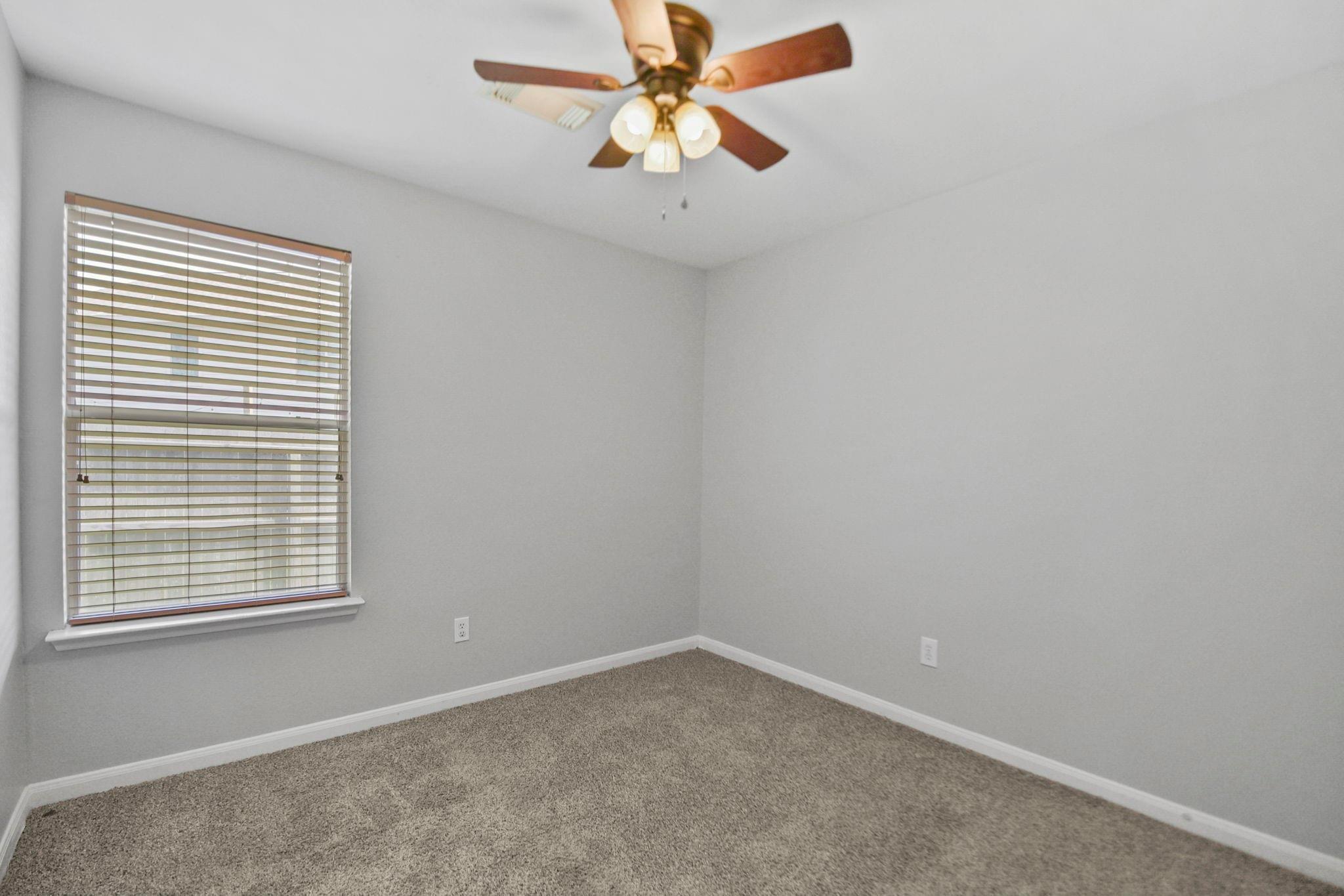 Empty bedroom with beige carpet, window blinds, and a wood-blade ceiling fan.