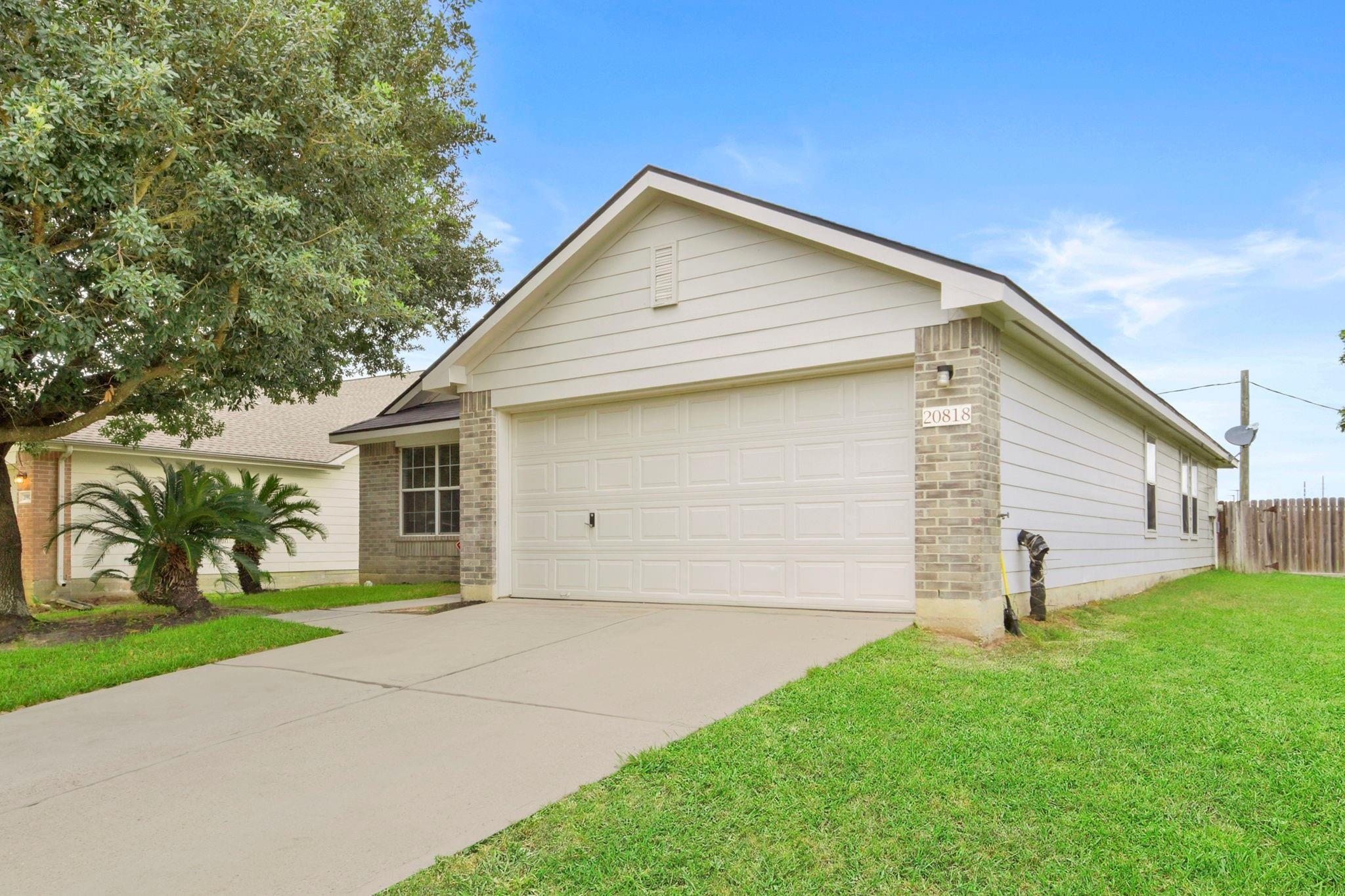 House exterior with a large double garage, brick accents, and a tree shading the driveway.