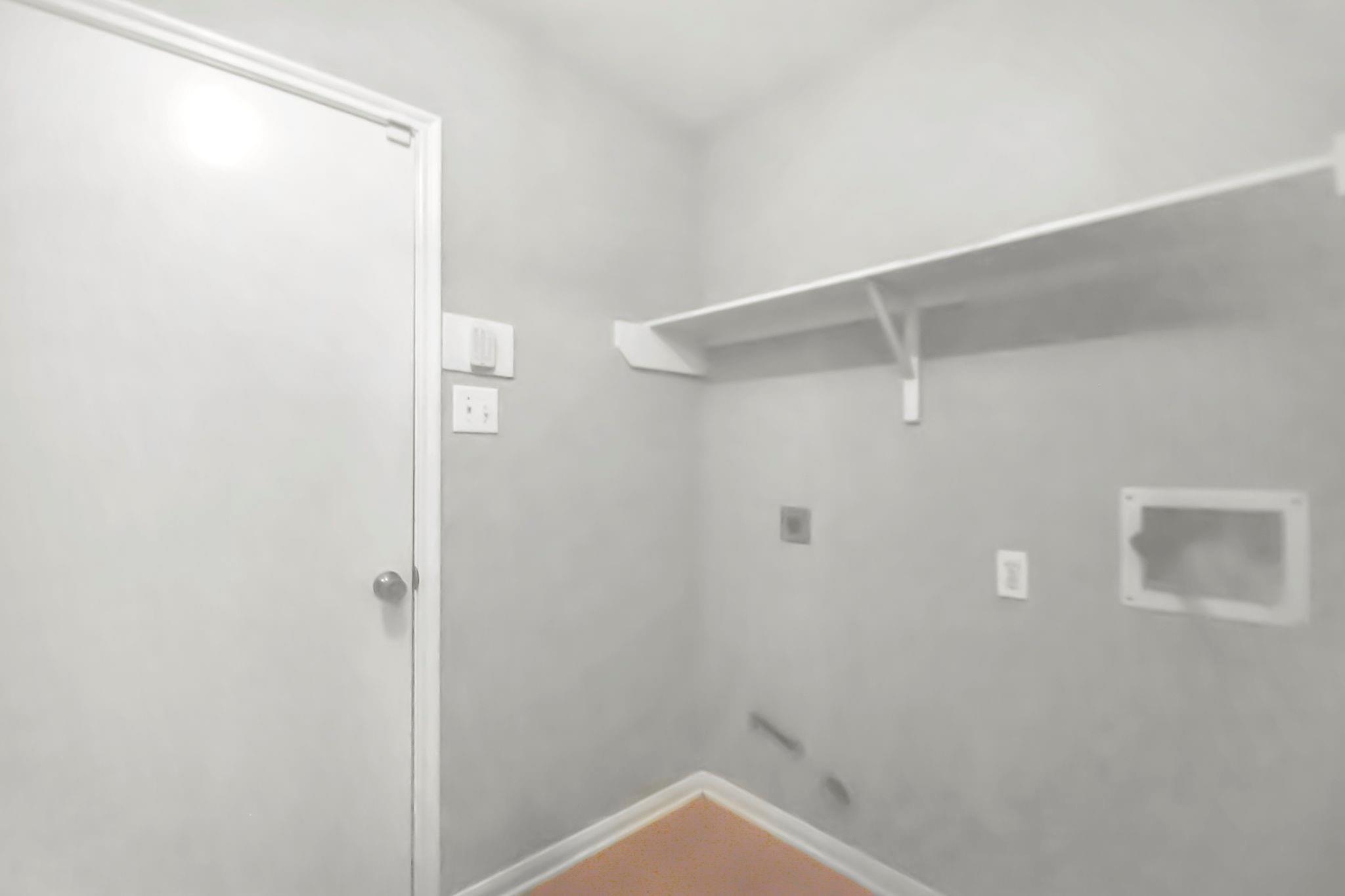 Empty laundry area with a long wall shelf, laundry connections, and vent fittings.