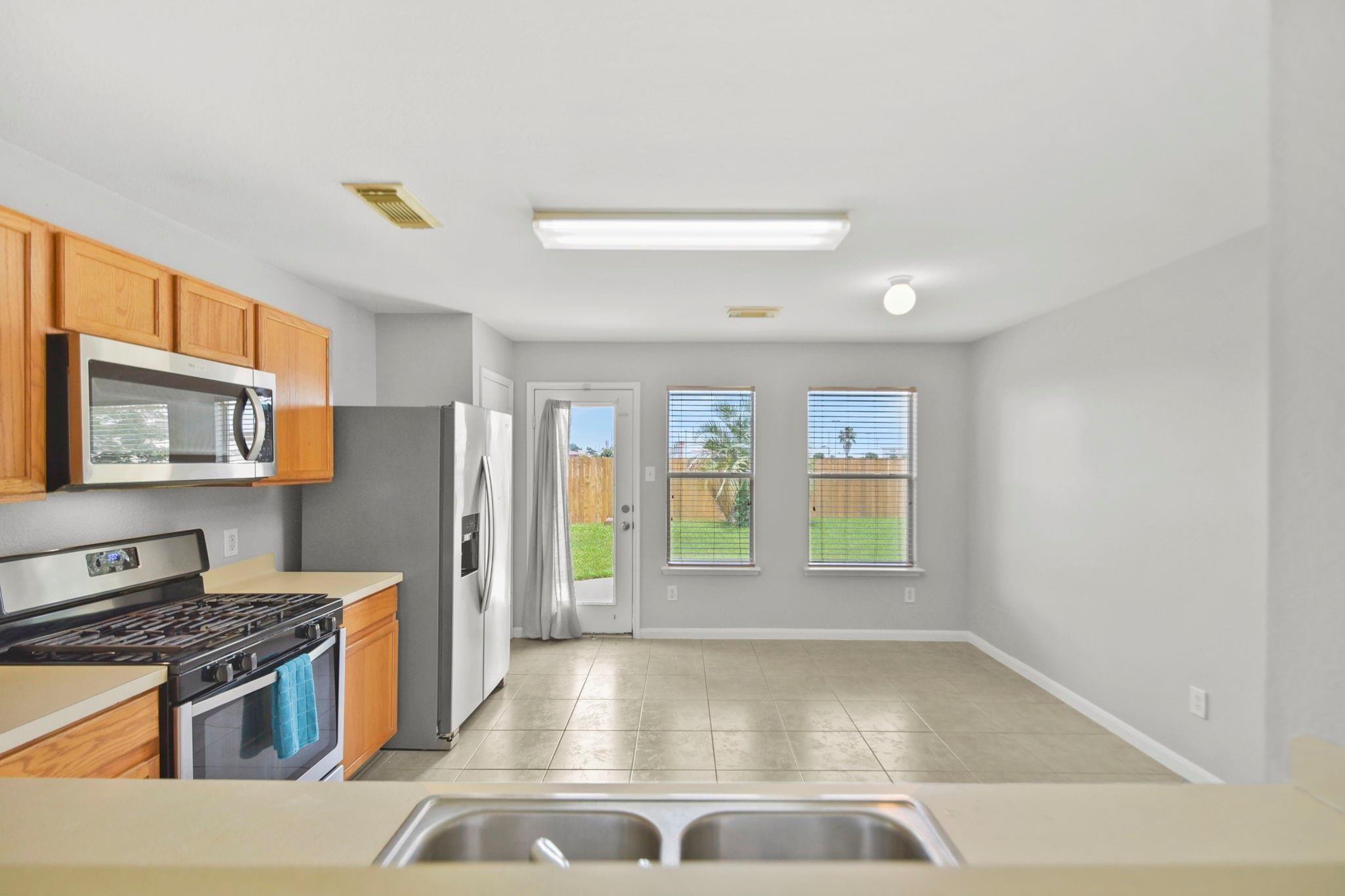 Kitchen with wood cabinets and stainless appliances, opening to a bright dining area overlooking the fenced backyard.