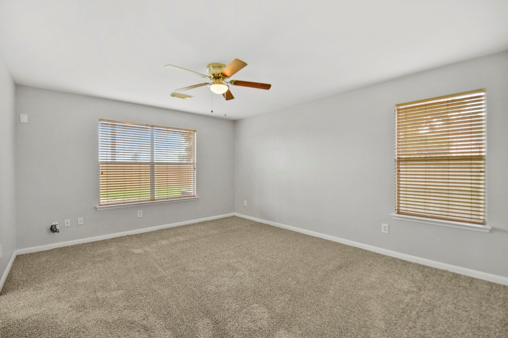 Empty carpeted bedroom with two windows and a ceiling fan with light.