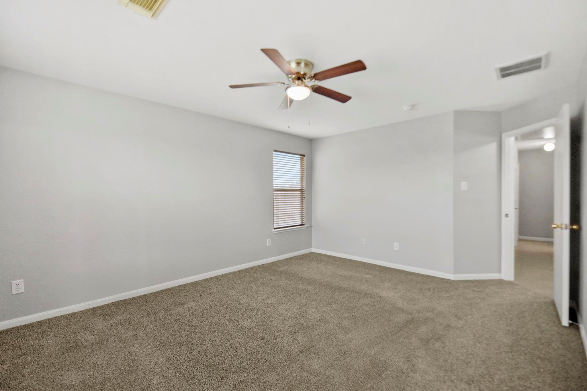 Empty carpeted room with gray walls, a ceiling fan, window blinds, and an open doorway.