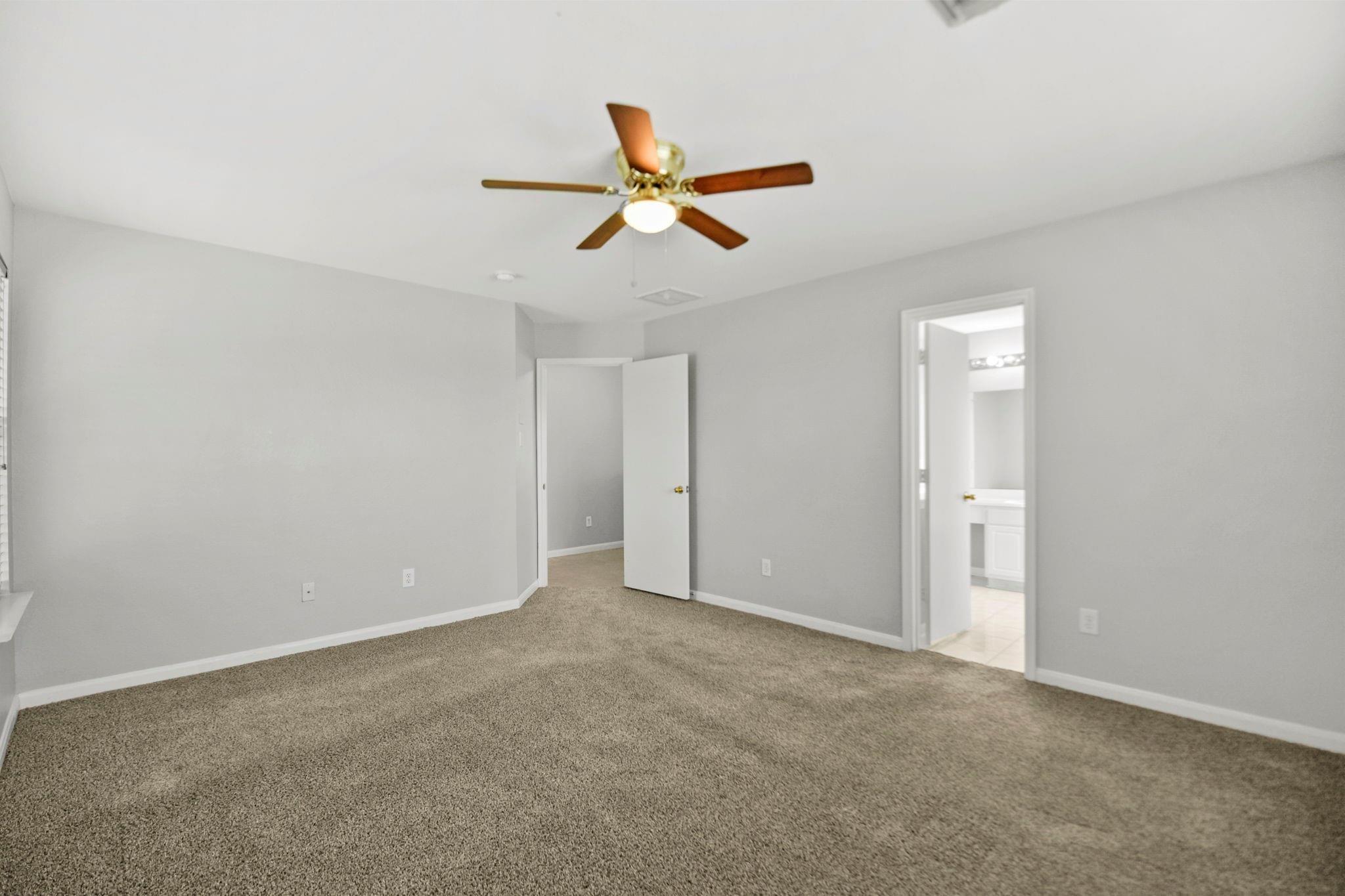 Empty carpeted bedroom with a ceiling fan and an open doorway to a bathroom.