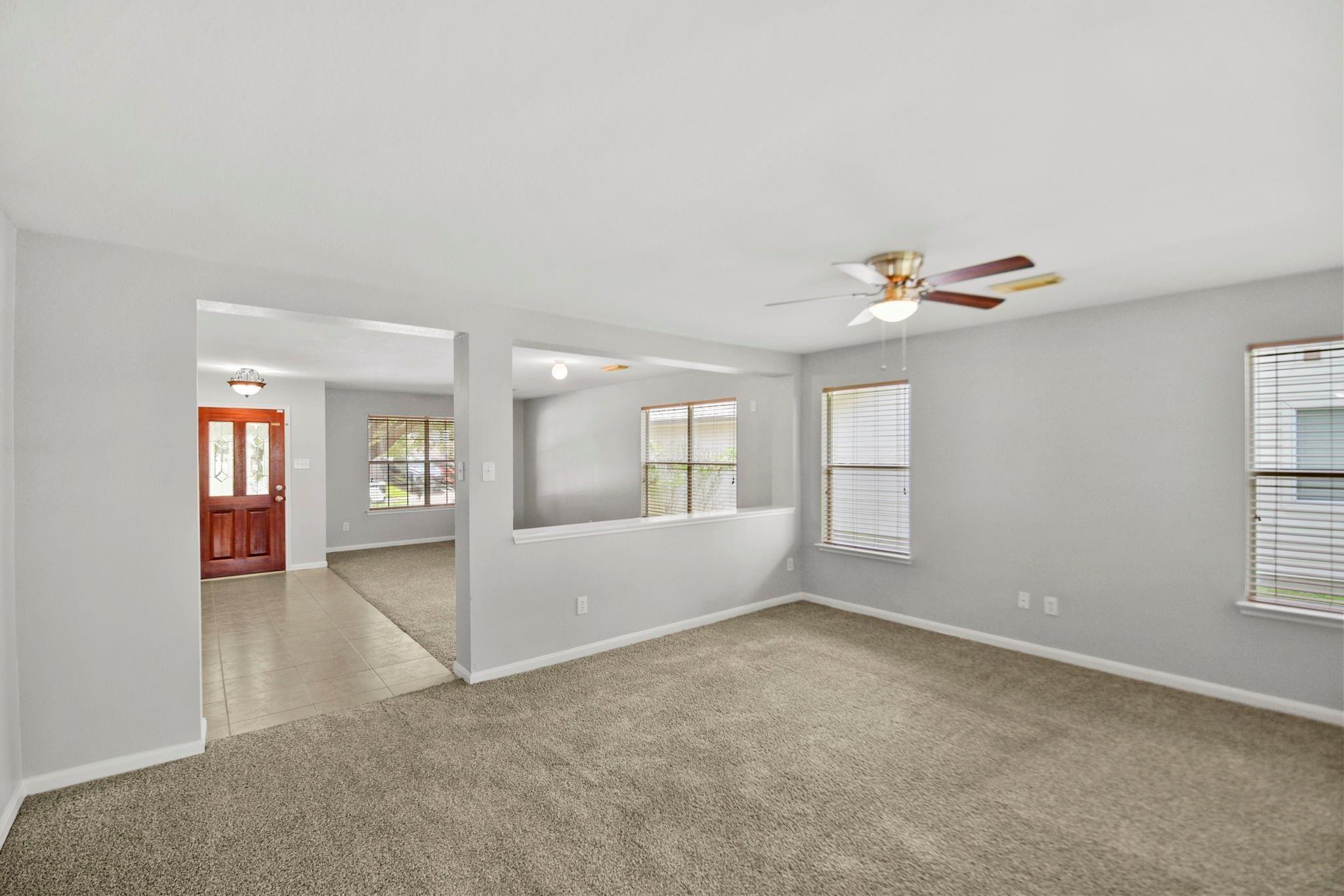 Unfurnished living room with beige carpet, a ceiling fan, and windows with blinds.