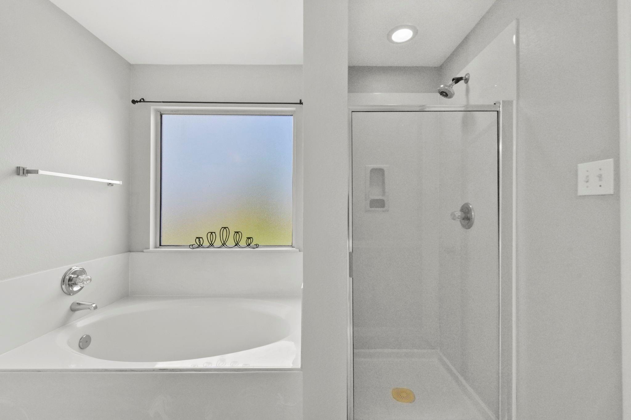 Bathroom with a soaking tub beneath a window and a separate glass-enclosed shower.