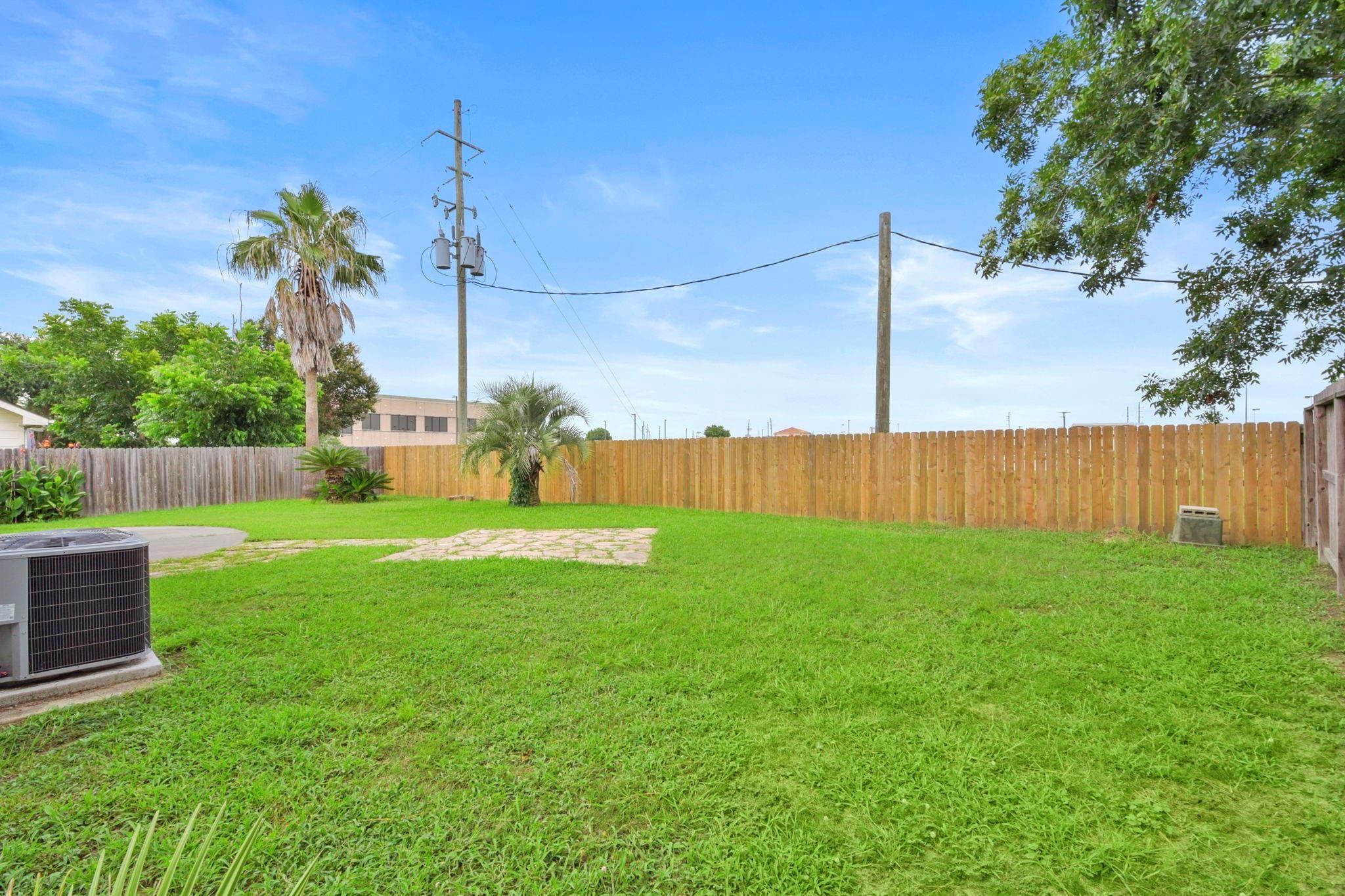 Backyard with a broad green lawn, wooden privacy fence, palm trees, and a small paved patio.