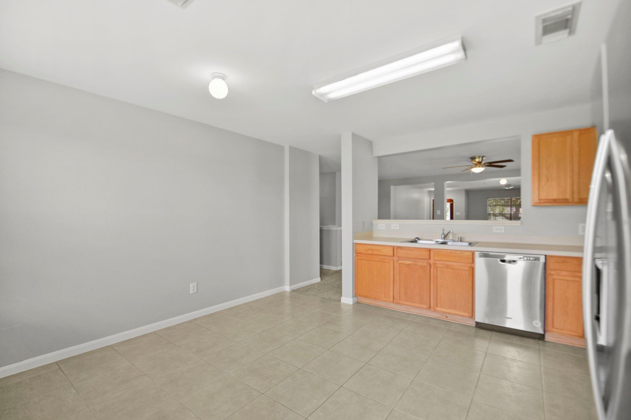 Empty kitchen with wood cabinets, stainless steel appliances, and beige tile flooring