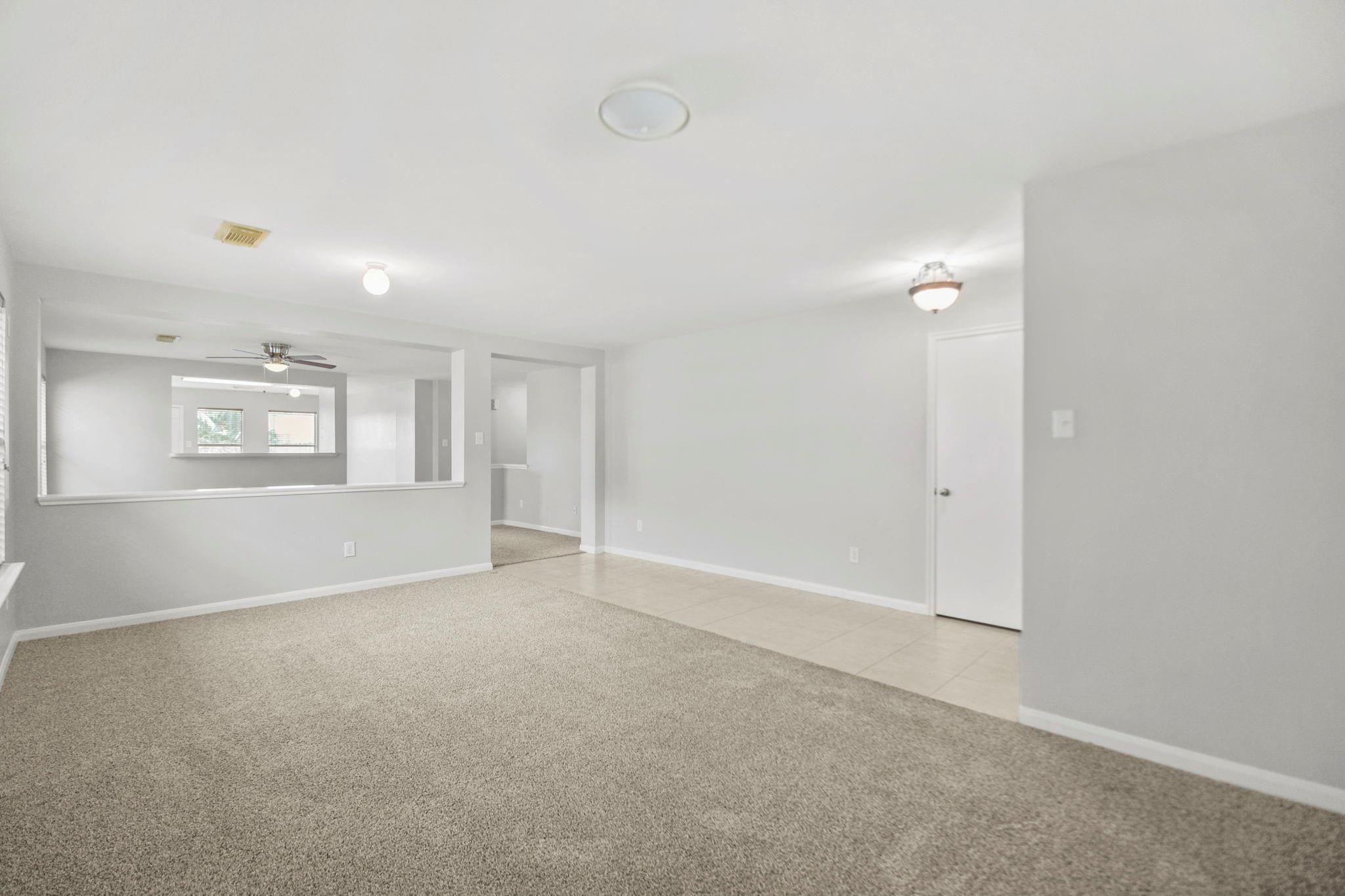 Vacant living room with beige carpet and a wide pass-through to an adjoining room.