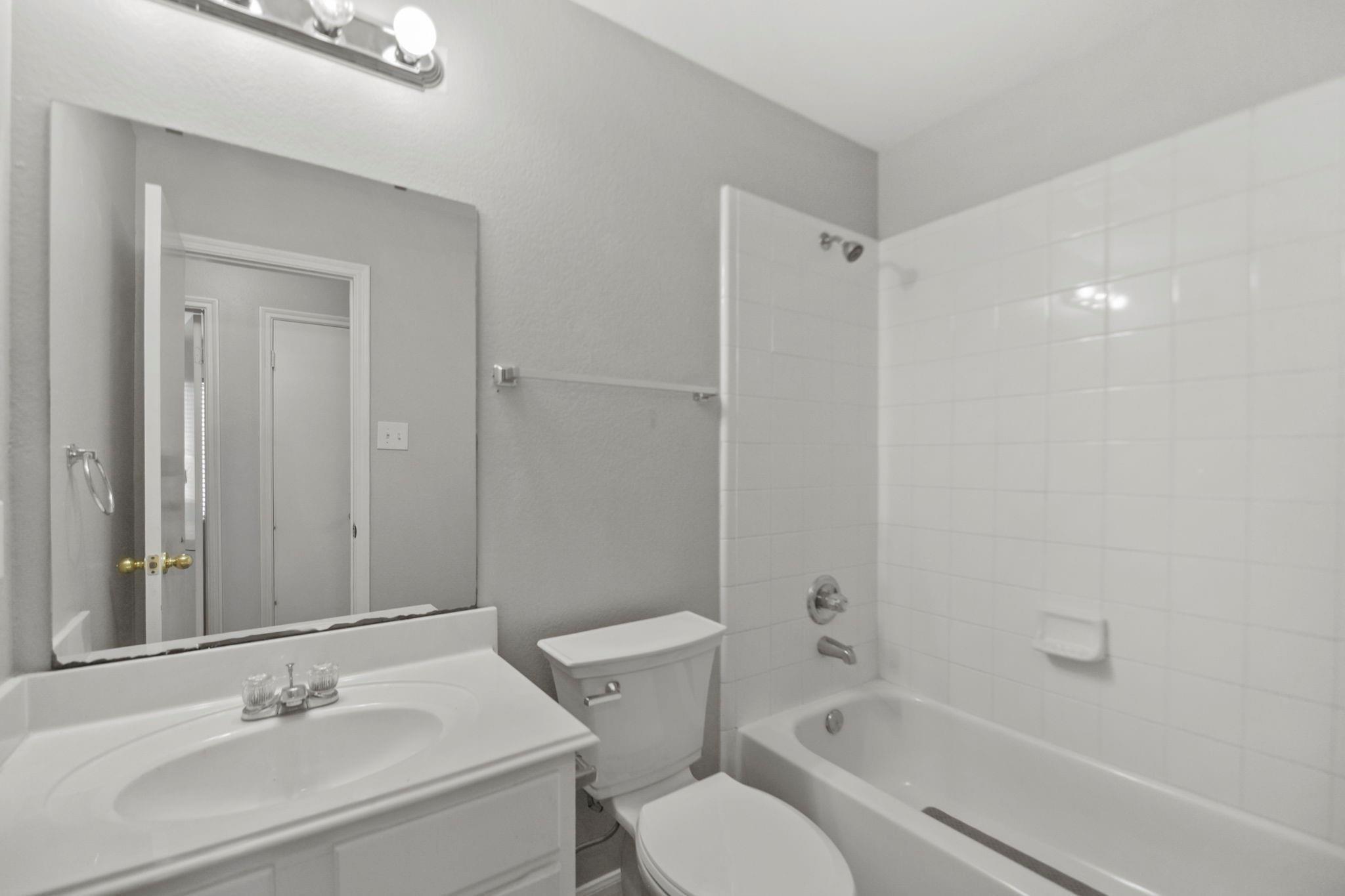 Bathroom with a white vanity, large mirror, toilet, and tiled bathtub and shower.