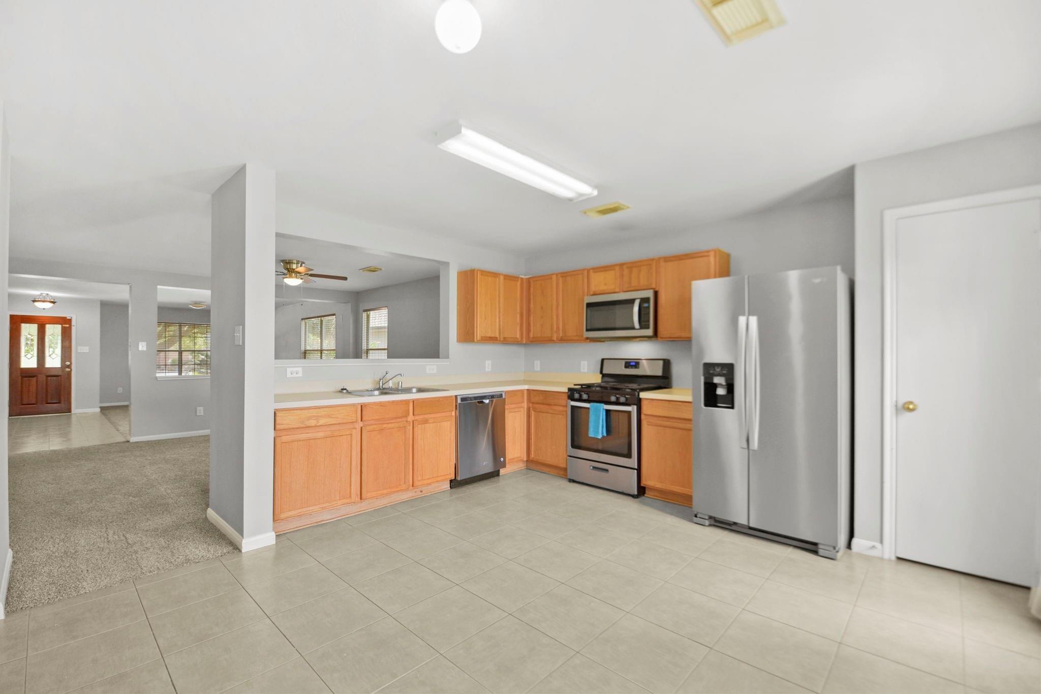 Kitchen with light wood cabinets, stainless steel appliances, and tiled flooring.