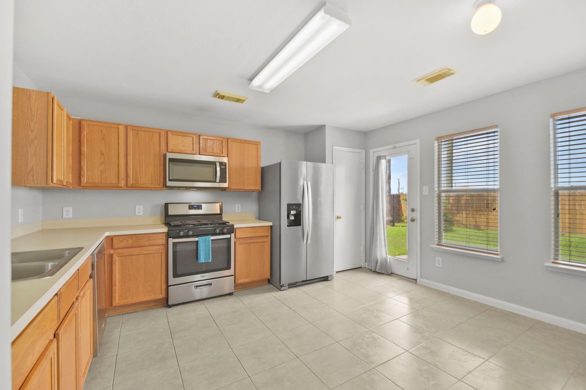 Kitchen with honey-colored cabinets, stainless steel appliances, and windows overlooking a fenced lawn.