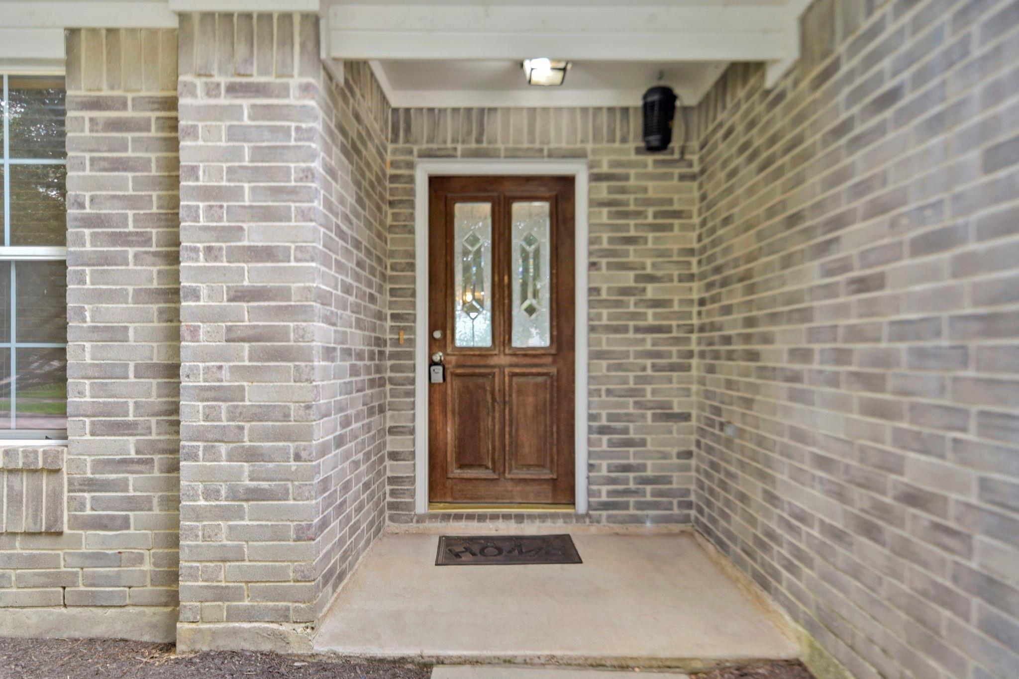 Brick home’s covered front entry with a brown double door and decorative glass panels.