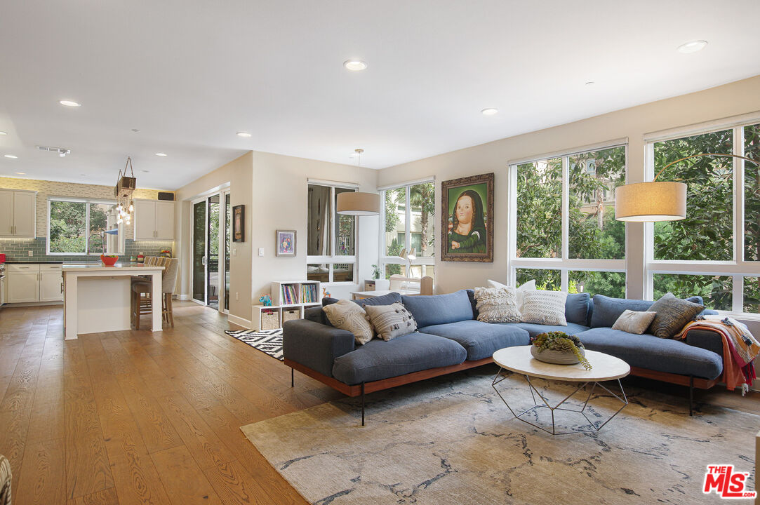 Open-plan living room with a blue sectional, large garden-facing windows, and a kitchen island.