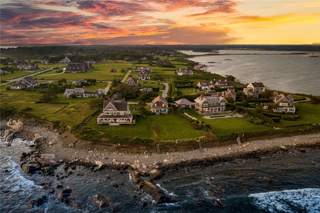 Aerial view of coastal homes along a rocky shore beneath a vivid sunset.
