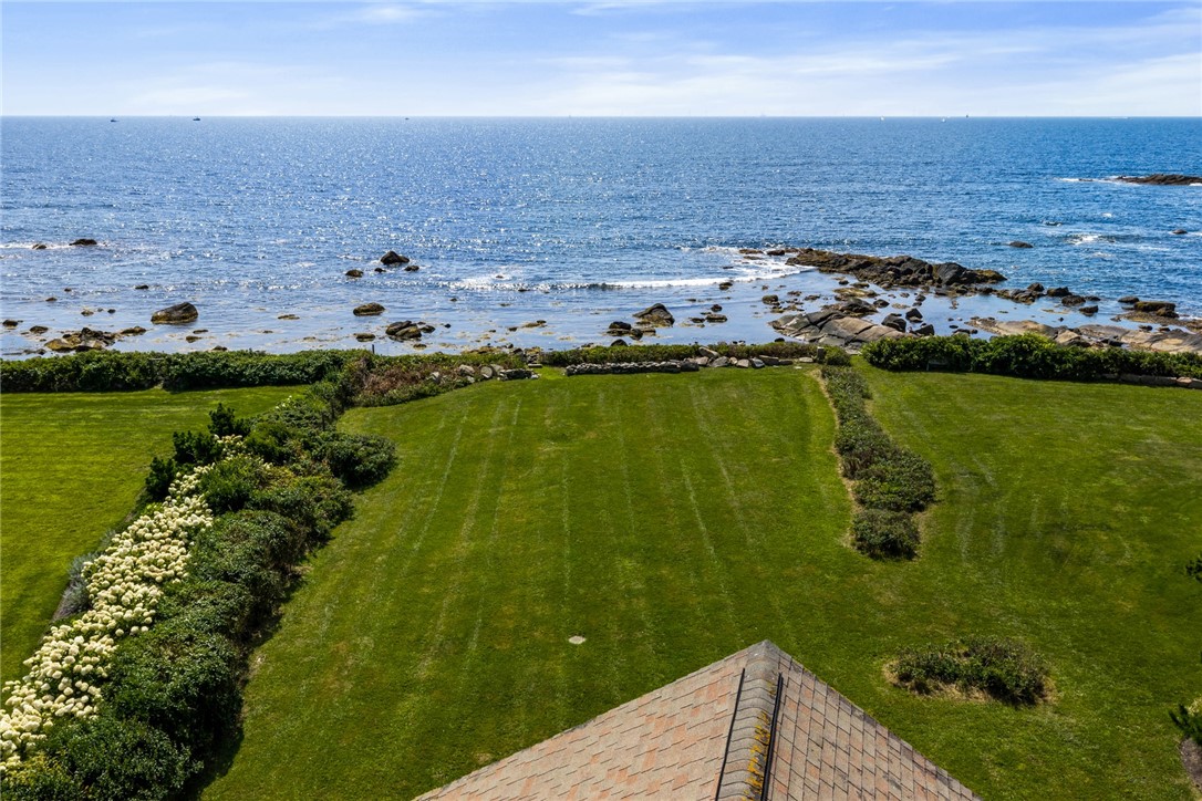 Aerial view of a landscaped lawn meeting a rocky ocean shore, with the house roof in the foreground.