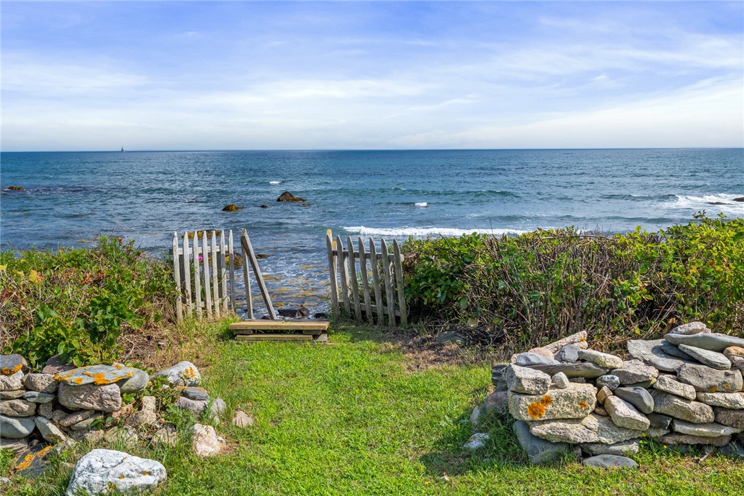 Grassy path and wooden gate opening to a rocky ocean shoreline.