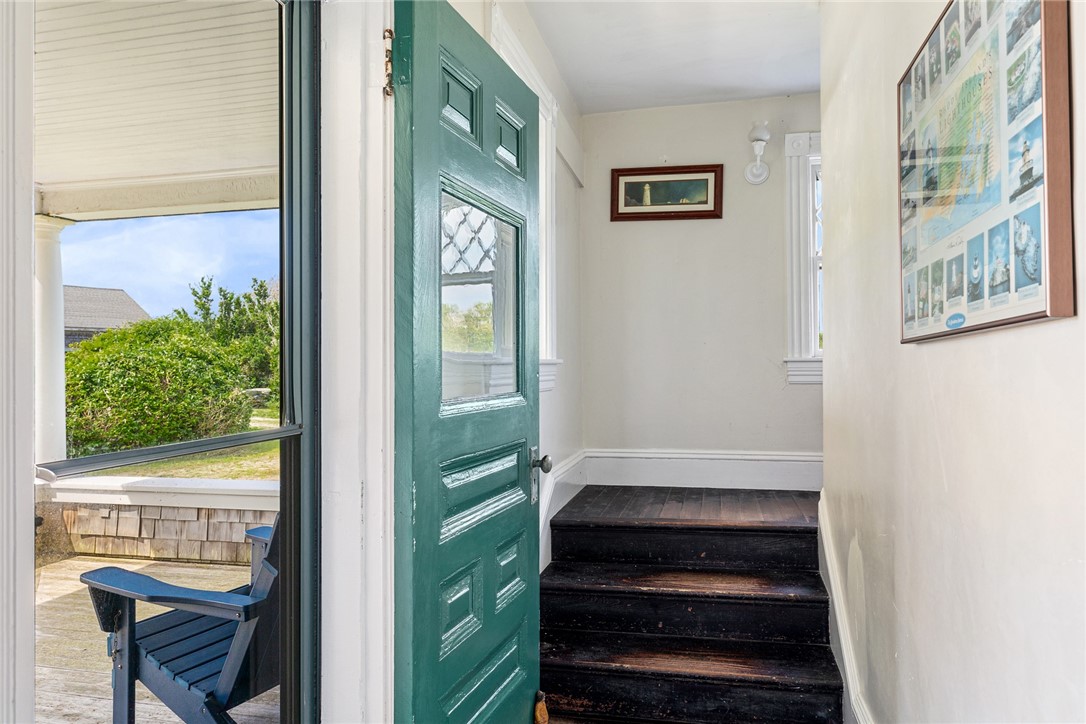 Entry hall with an open teal-green door, dark wooden steps, and a window overlooking a blue chair and greenery.