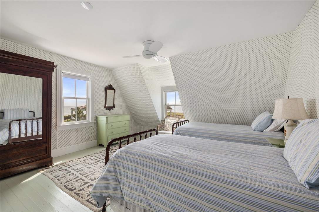 Bedroom with two striped beds, patterned wallpaper, and a dark wood mirrored armoire.