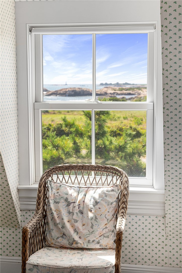 Wicker chair beside a window overlooking coastal greenery, rocky shore, and water.