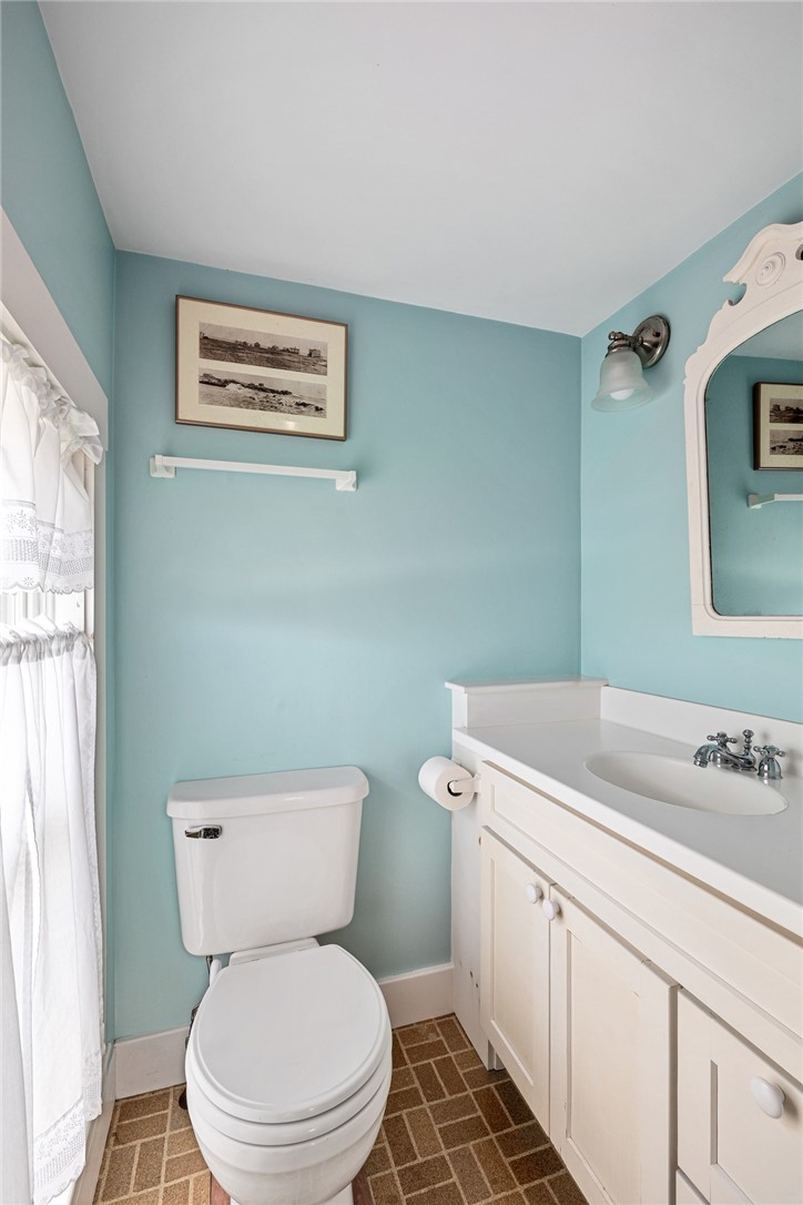 Bathroom with pale aqua walls, white vanity, decorative mirror, and lace window curtain.