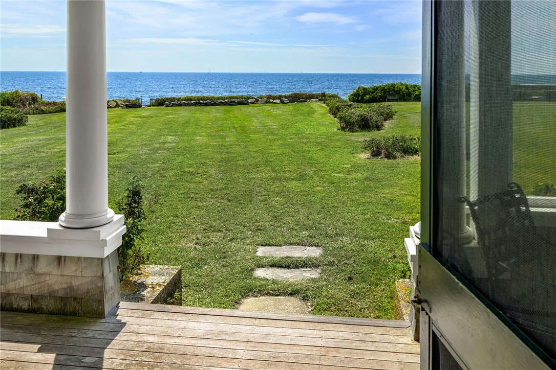 Lawn stretching from a wooden porch to the ocean, bordered by a low stone wall.