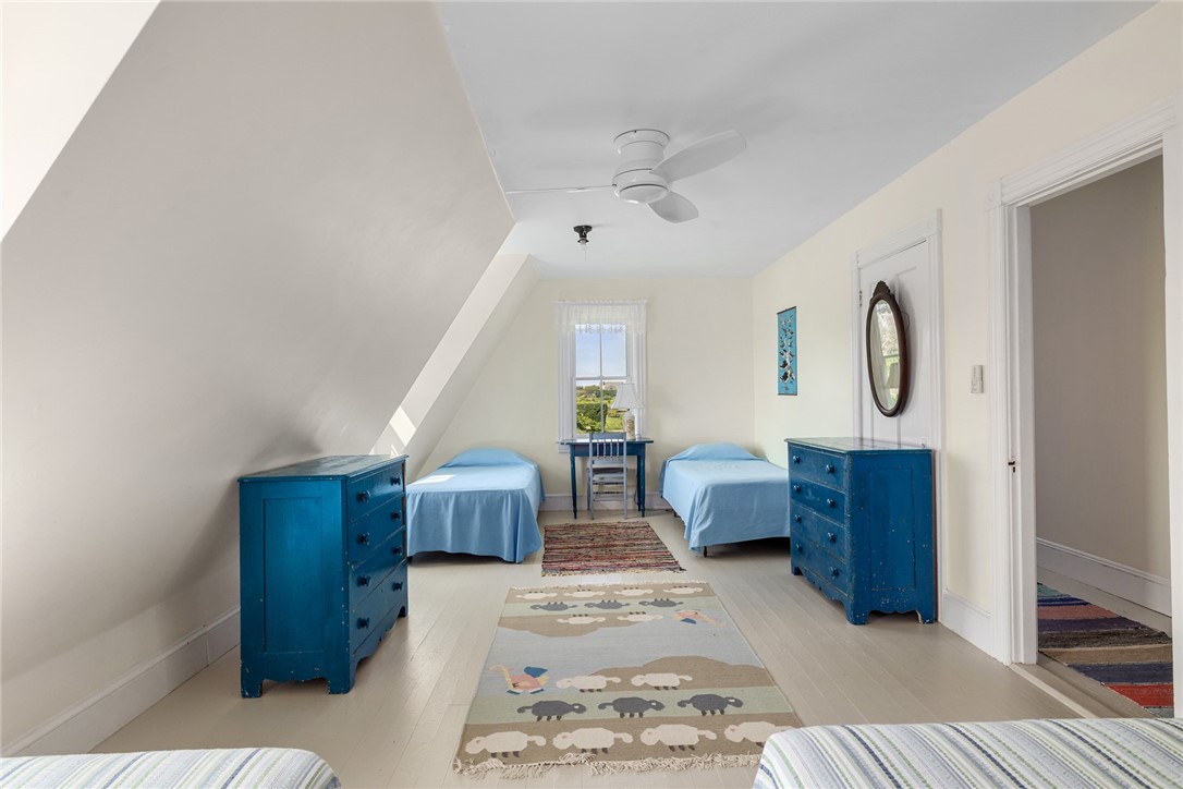 Attic bedroom with two blue-dressed twin beds, blue dressers, and a window overlooking greenery.
