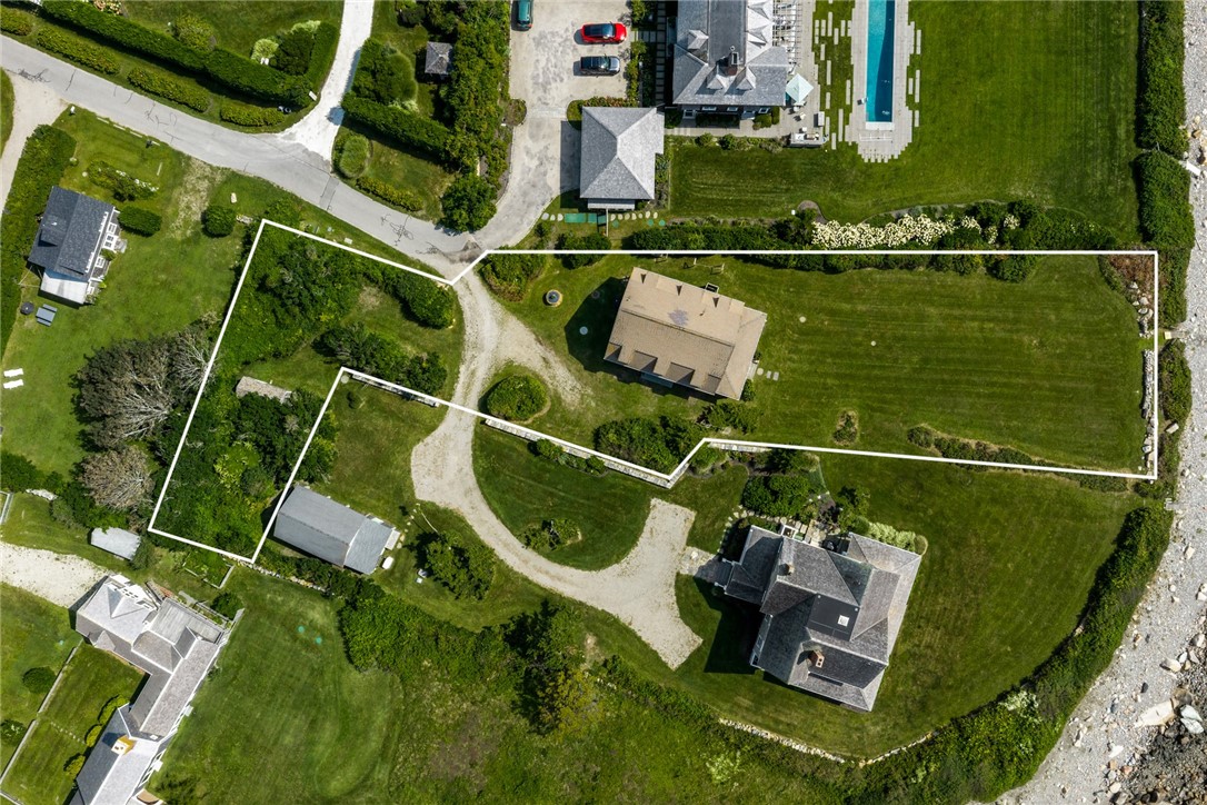 Aerial view of a home and landscaped lot outlined in white beside a rocky shoreline.