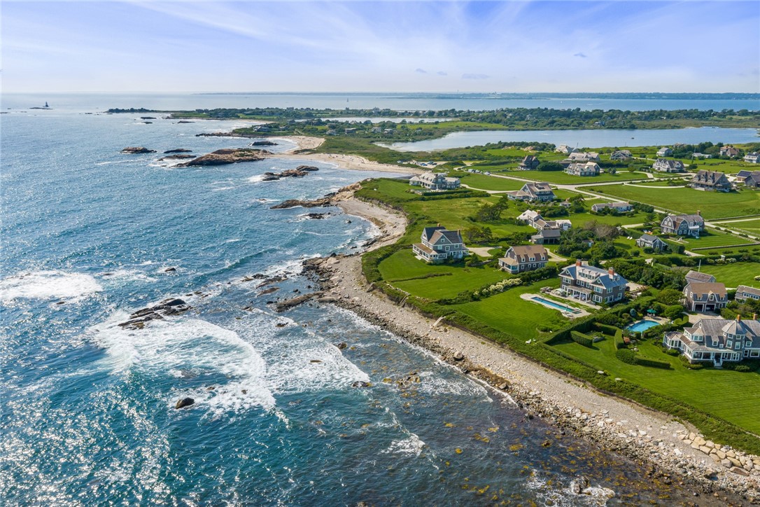 Aerial view of coastal homes beside a rocky shoreline and blue water.