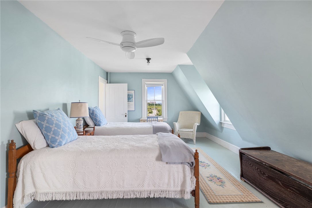 Attic bedroom with two twin beds, pale blue walls, and a window overlooking greenery.
