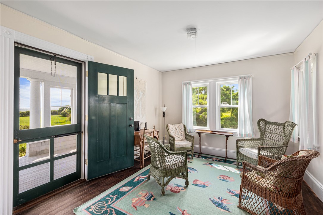Sunroom with wicker chairs, a floral rug, and green doors opening toward the ocean.