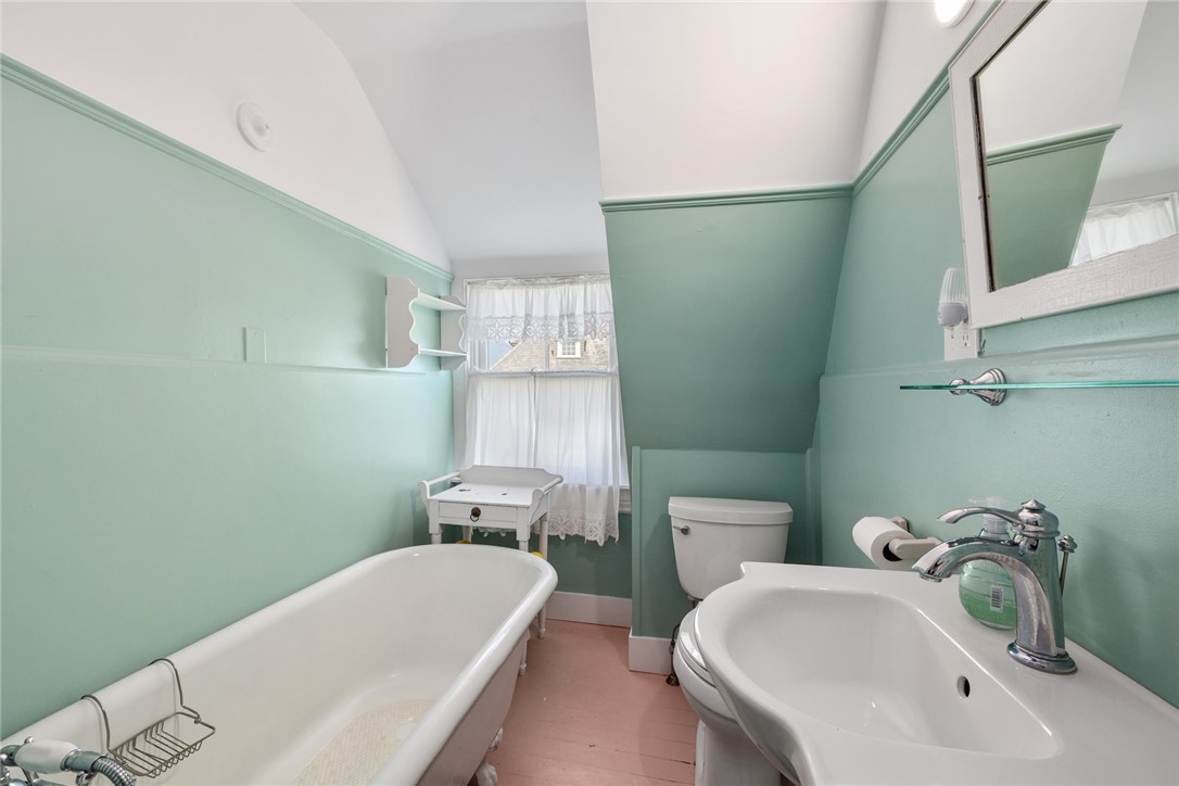 Bathroom with mint-green walls, clawfoot tub, pedestal sink, and curtained window.