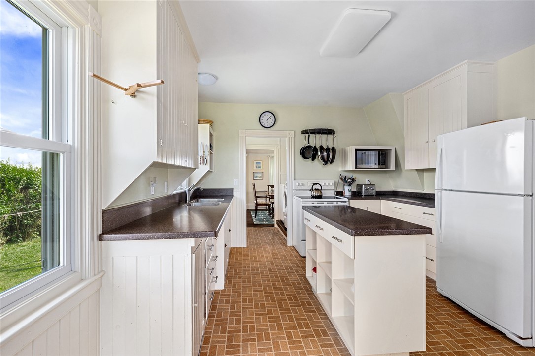 Kitchen with white cabinets, dark countertops, central island, and a large window overlooking greenery.