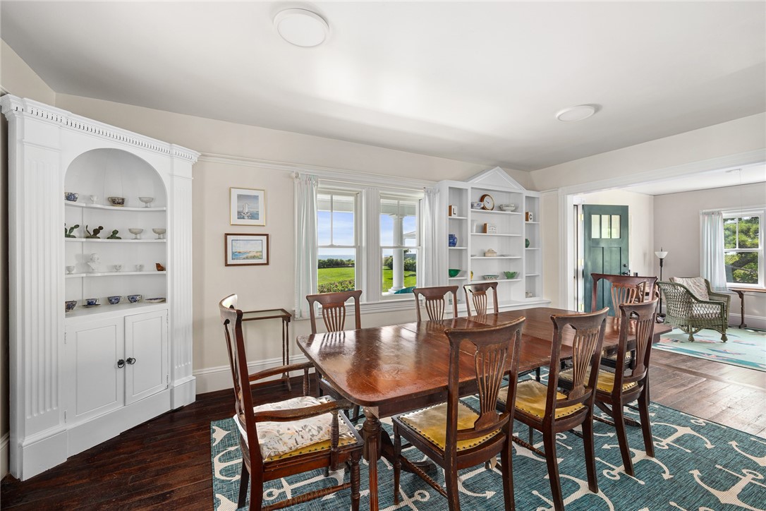Dining room with a long wooden table, white built-ins, and a view of water through the windows.