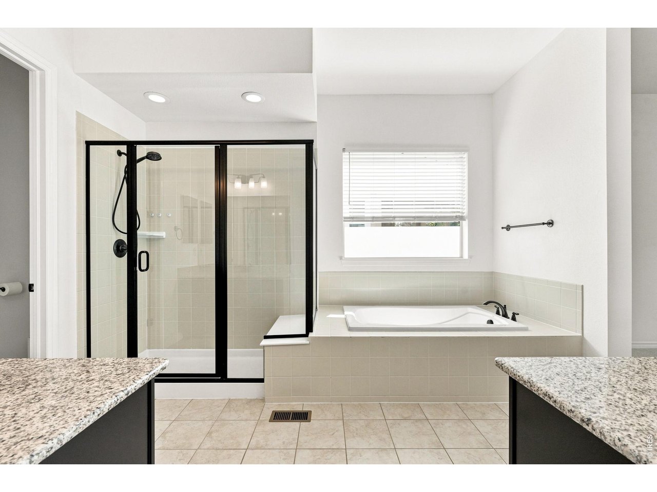 Bathroom with a black-framed glass shower, built-in tub, and granite vanity counters.