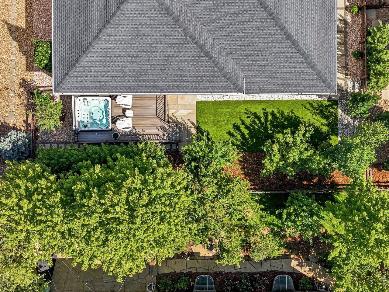 Aerial view of a landscaped backyard with a hot tub on a deck beside the home.