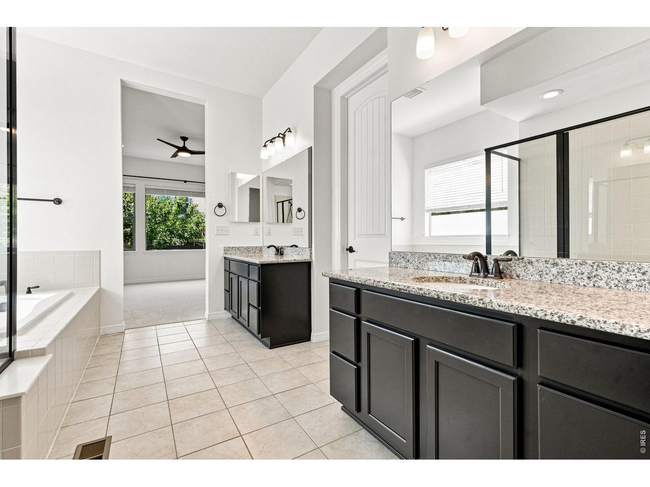Bathroom with dark double vanity, speckled stone counters, tiled soaking tub, and glass shower.