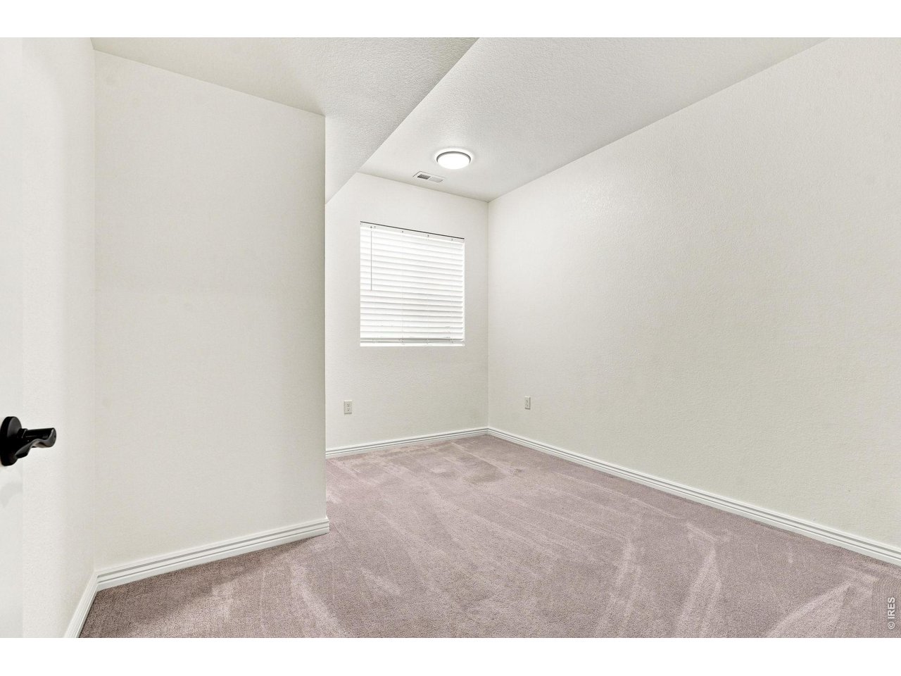 Empty bedroom with mauve carpet, a window with closed blinds, and a recessed ceiling light.