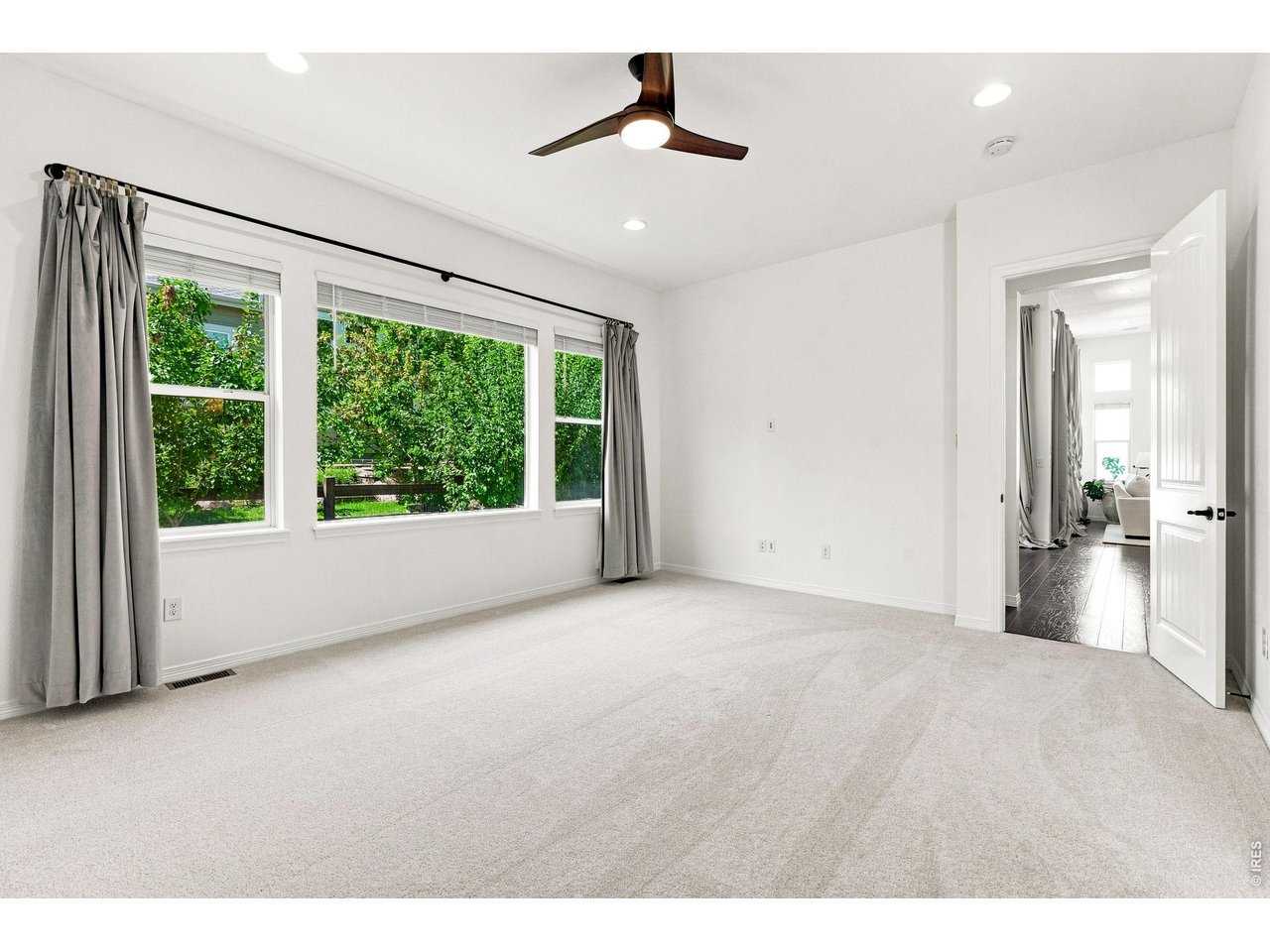 Vacant bedroom with light carpet, three curtained windows, and a ceiling fan.