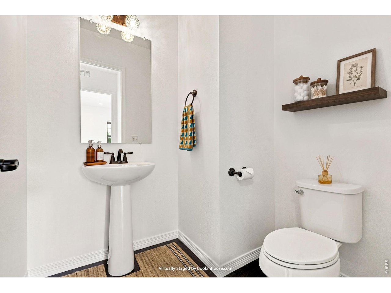 Powder room with a pedestal sink, large mirror, toilet, and dark floating shelf.