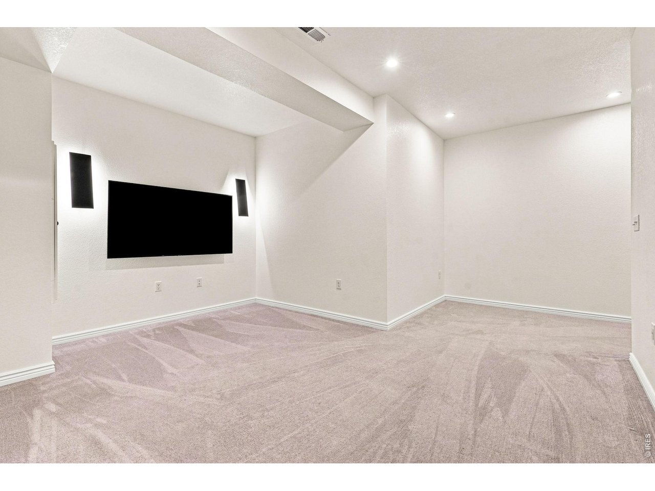 Empty media room with a built-in screen, wall speakers, and light carpeting.
