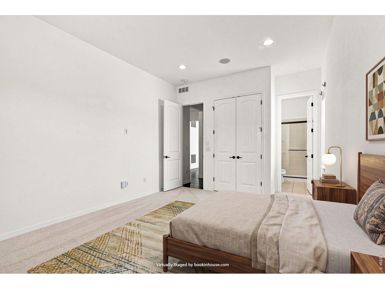 Virtually staged bedroom with a large bed, patterned rug, double closet doors, and an ensuite bathroom doorway.