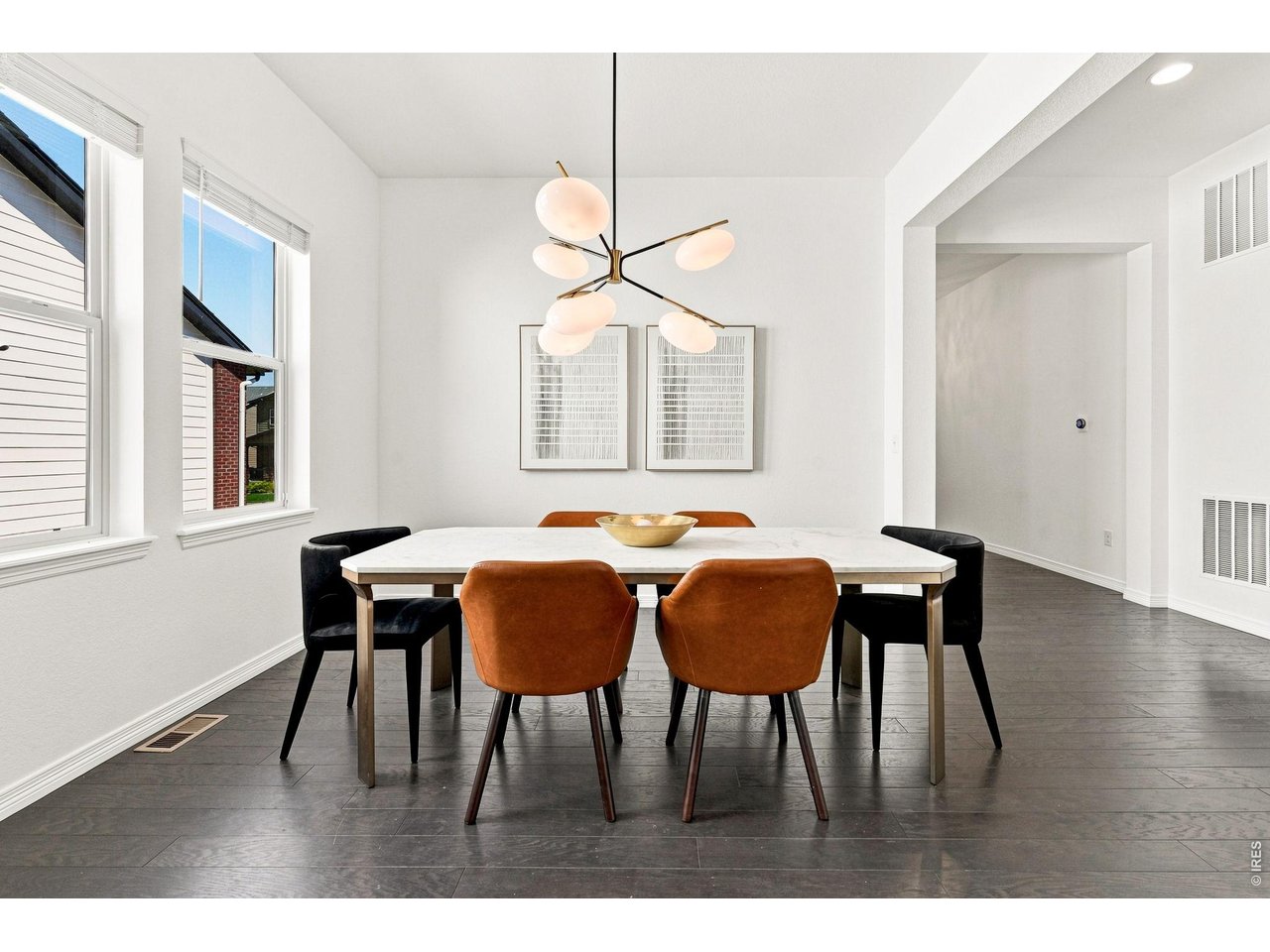 Dining room with a white table, rust-colored chairs, dark floors, and a modern chandelier.